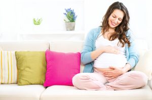 A woman sitting on the couch while holding her baby bump