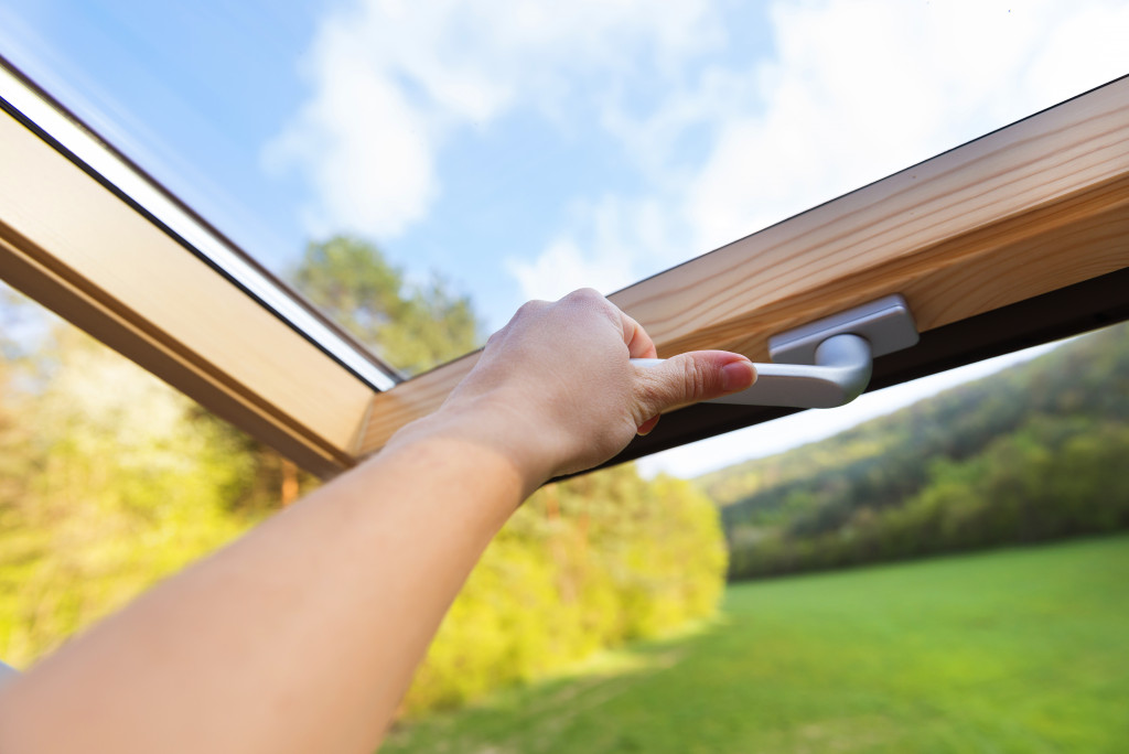 A hand opening a skylight on a bright, sunny day