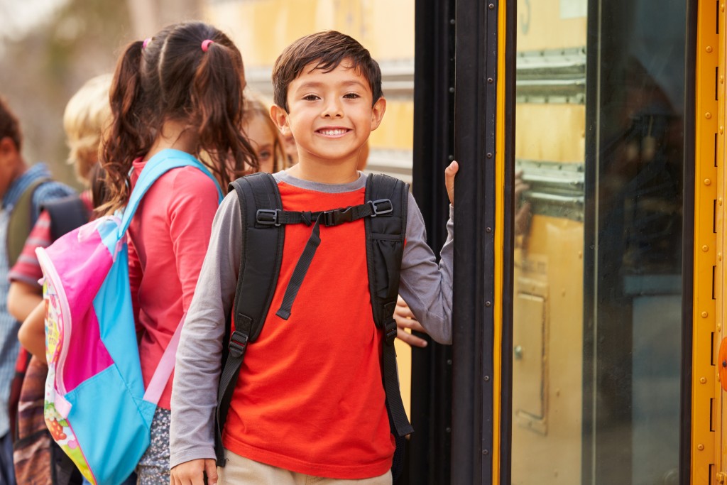 Young boy standing outside a school bus.