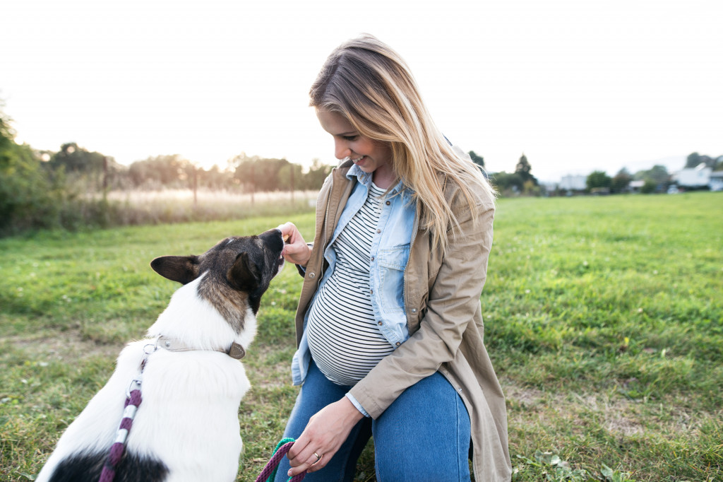 pregnant woman smiling while playing with pet dog outdoors