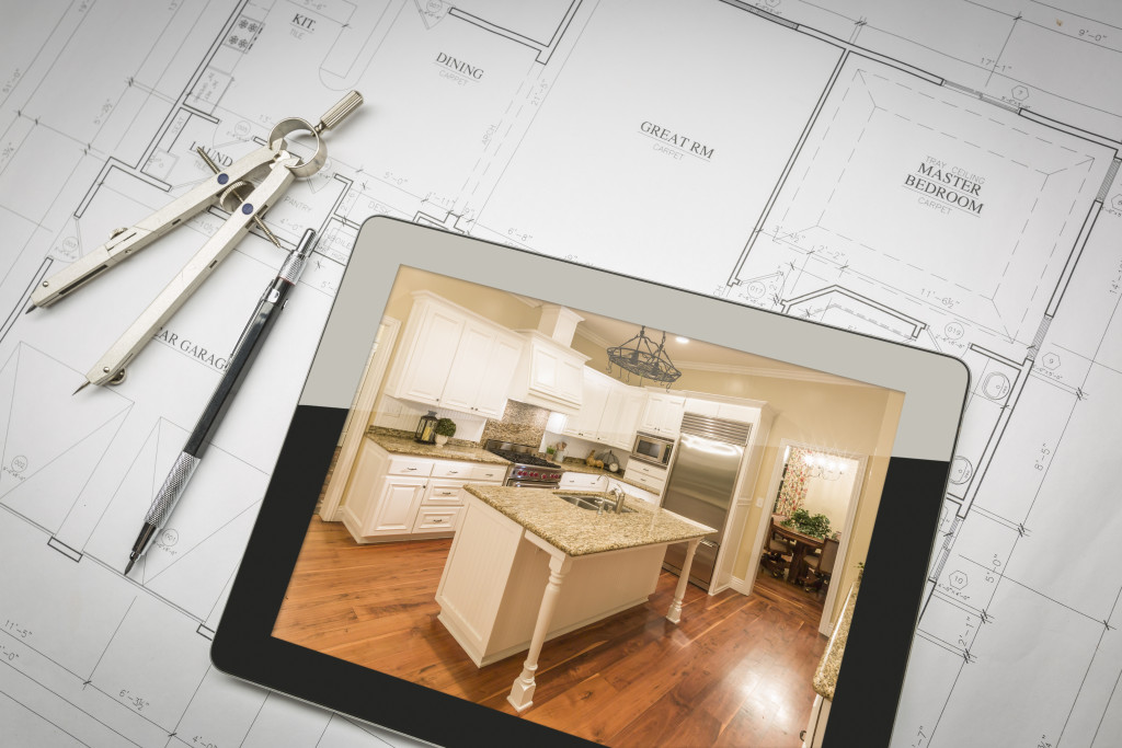 a picture of kitchen in the tablet on top of renovation plans beside compass and pen