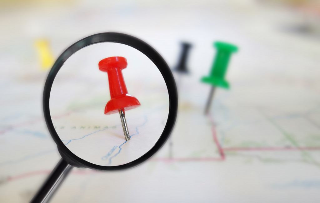 red push pin under small magnifying glass with map as base