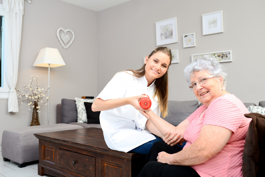 young woman helping elderly woman exercise at home