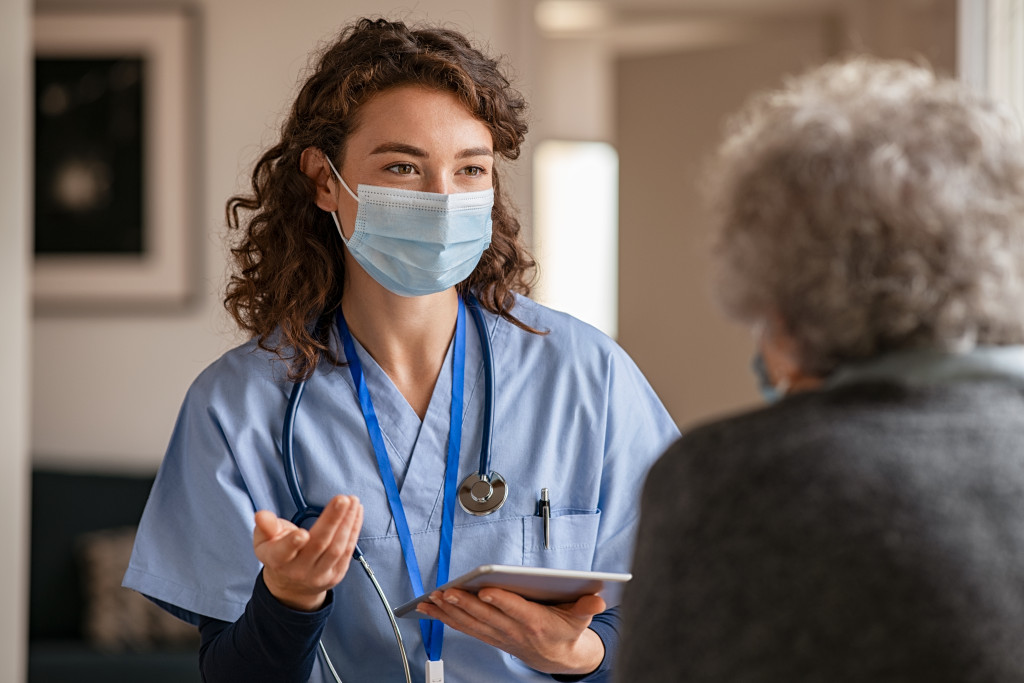 young nurse with stethoscope and tablet talking to elderly parent