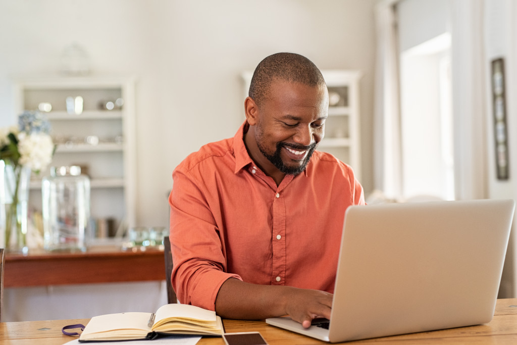 man smiling while researching in his laptop about the country