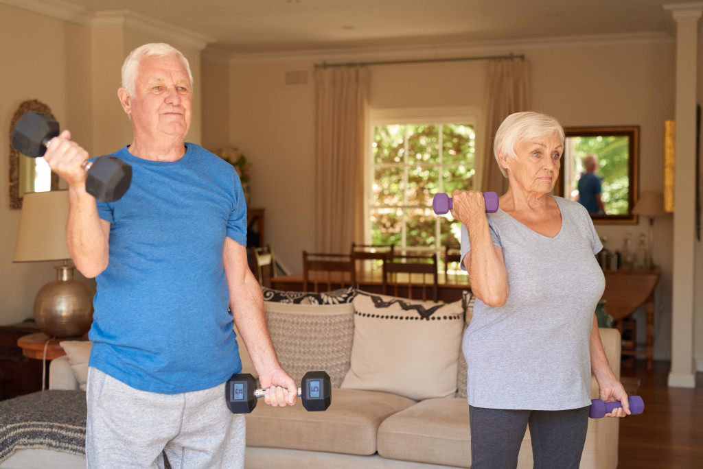 Senior couple exercise in the living room of a house using dumbbells.