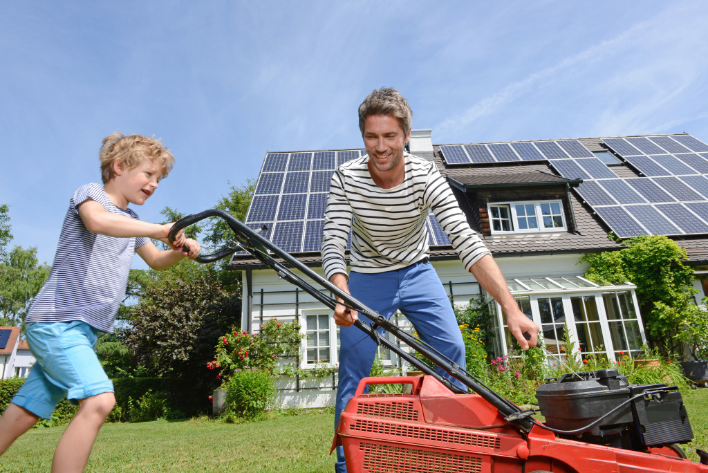 Young boy using a lawnmower with his dad guiding him.