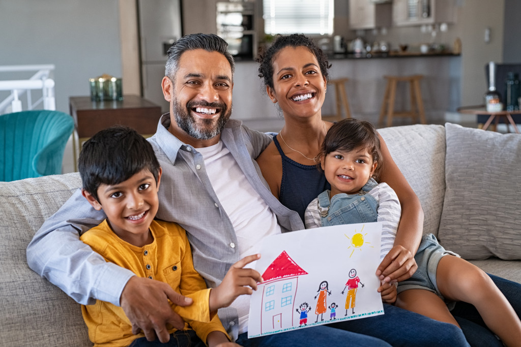 Family sitting on a sofa at home while showing a drawing of their children.